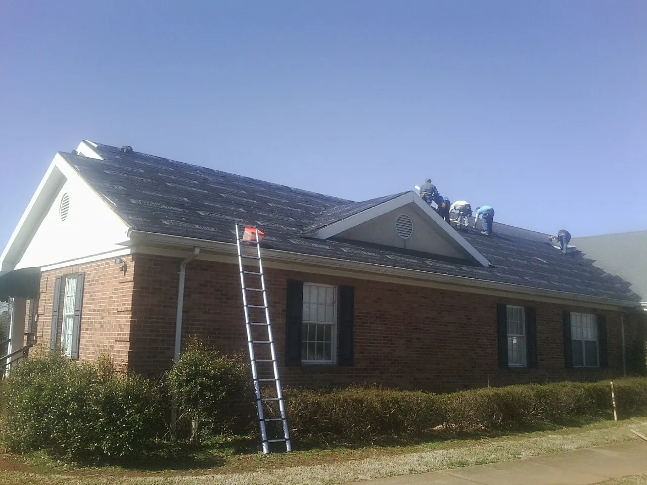 Crew tearing shingles off a brick ranch roof with a ladder set — Emergency Roof Repair work by our crew in Homerville