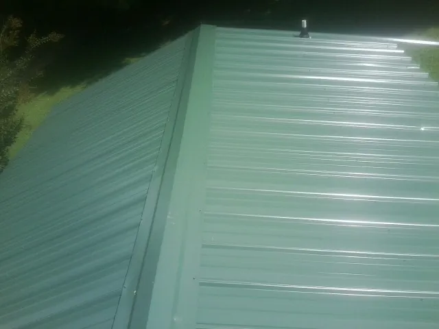 New green metal panels meeting at the ridge of a roof — Flat Roof Repair work by our crew in Homerville
