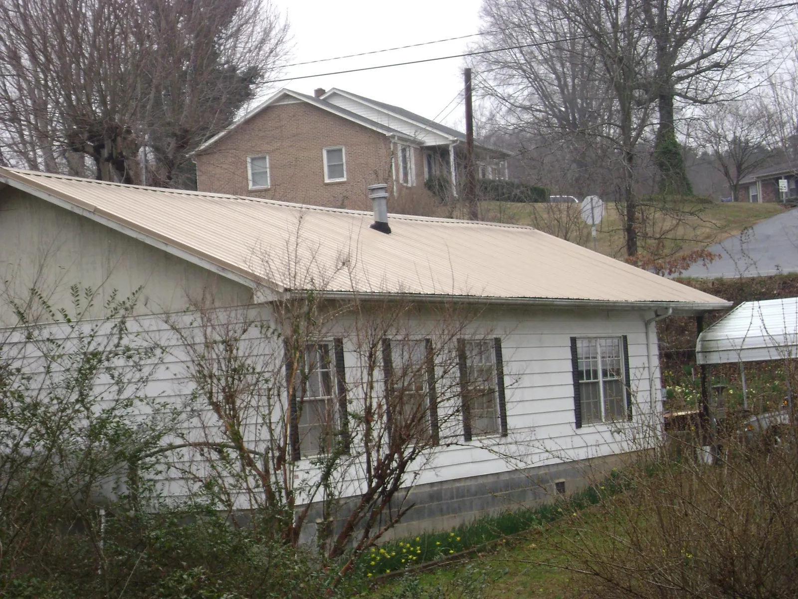 Tan metal roof on a white sided house set into a hillside — Commercial Roofing by Roofing Brothers in Homerville