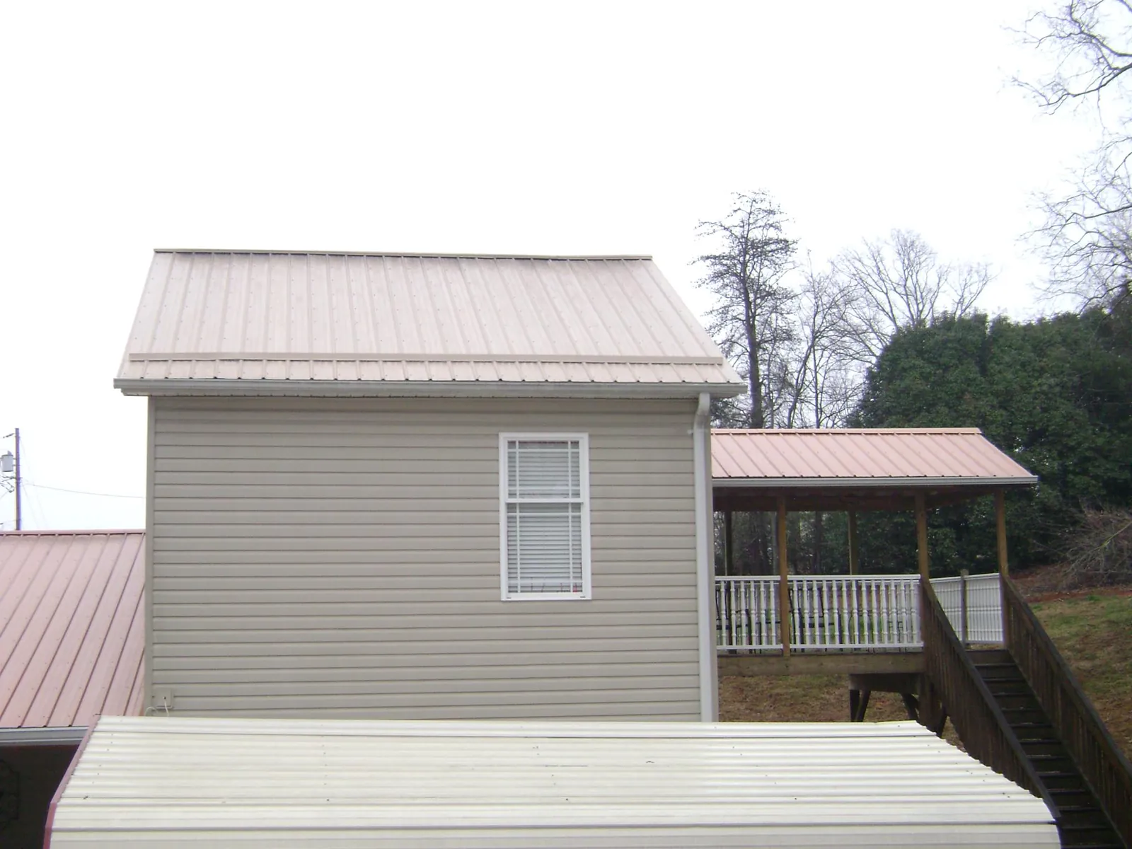 Tan metal roofs on a two story addition and attached porch, from a Roof Replacement job in Homerville